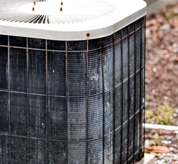Old outdoor HVAC unit with rusted casing and overgrown surroundings, showing signs of age and wear